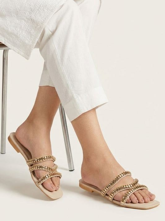 Gold embellished sandals worn with white pants on a light background