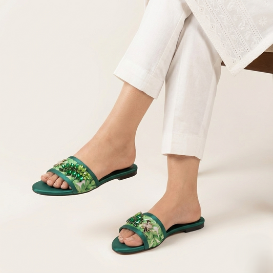 Green sandals with floral patterns worn by a person on a light background